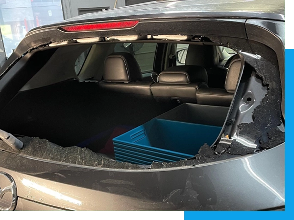 A car with its rear window shattered, exposing the interior.
