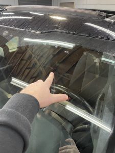 A person pointing at a car windshield in a garage.