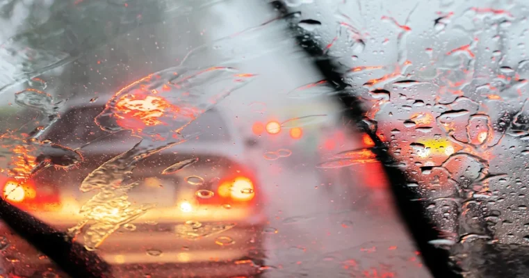 View through a rain-drenched car windshield with blurred traffic lights.