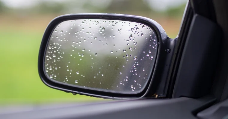 Close-up of a car's side view mirror with raindrops on it.
