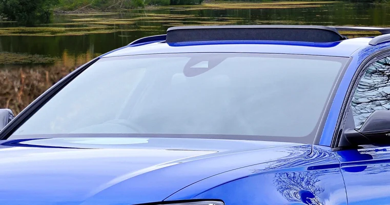 A car with a pristine windshield parked by a tranquil lakeside.
