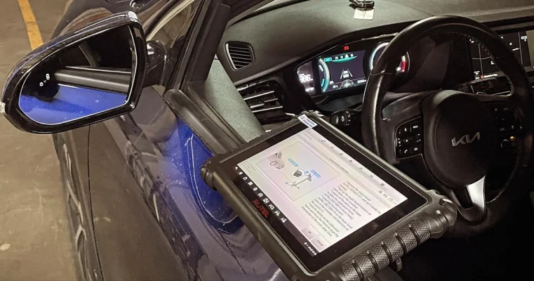 Interior of a Kia vehicle during an ADAS calibration process with a tablet displaying instructions.